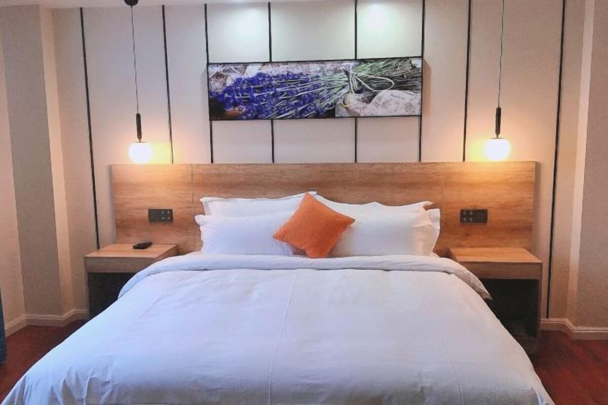 A neatly made bed with white linens and an orange pillow, flanked by two bedside tables with lamps.