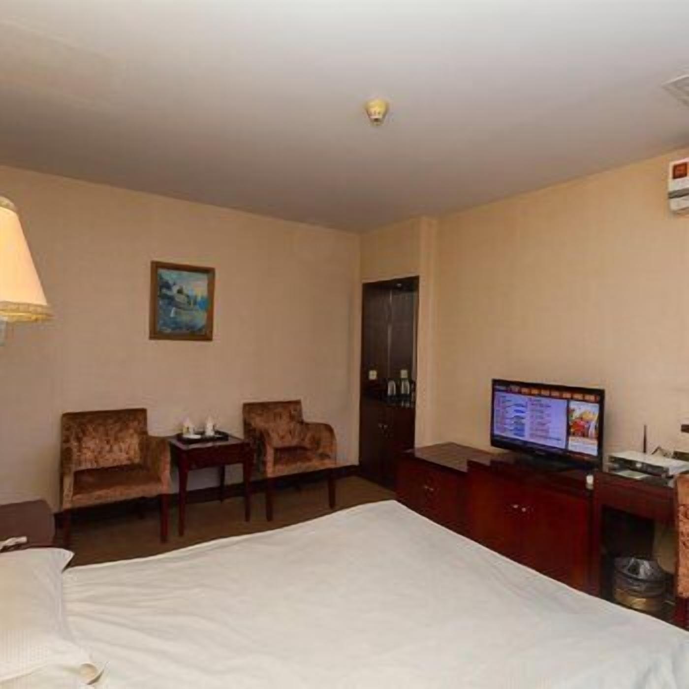 Habitación de hotel con una cama, dos sillones, una mesita, un televisor y un cuadro en la pared.