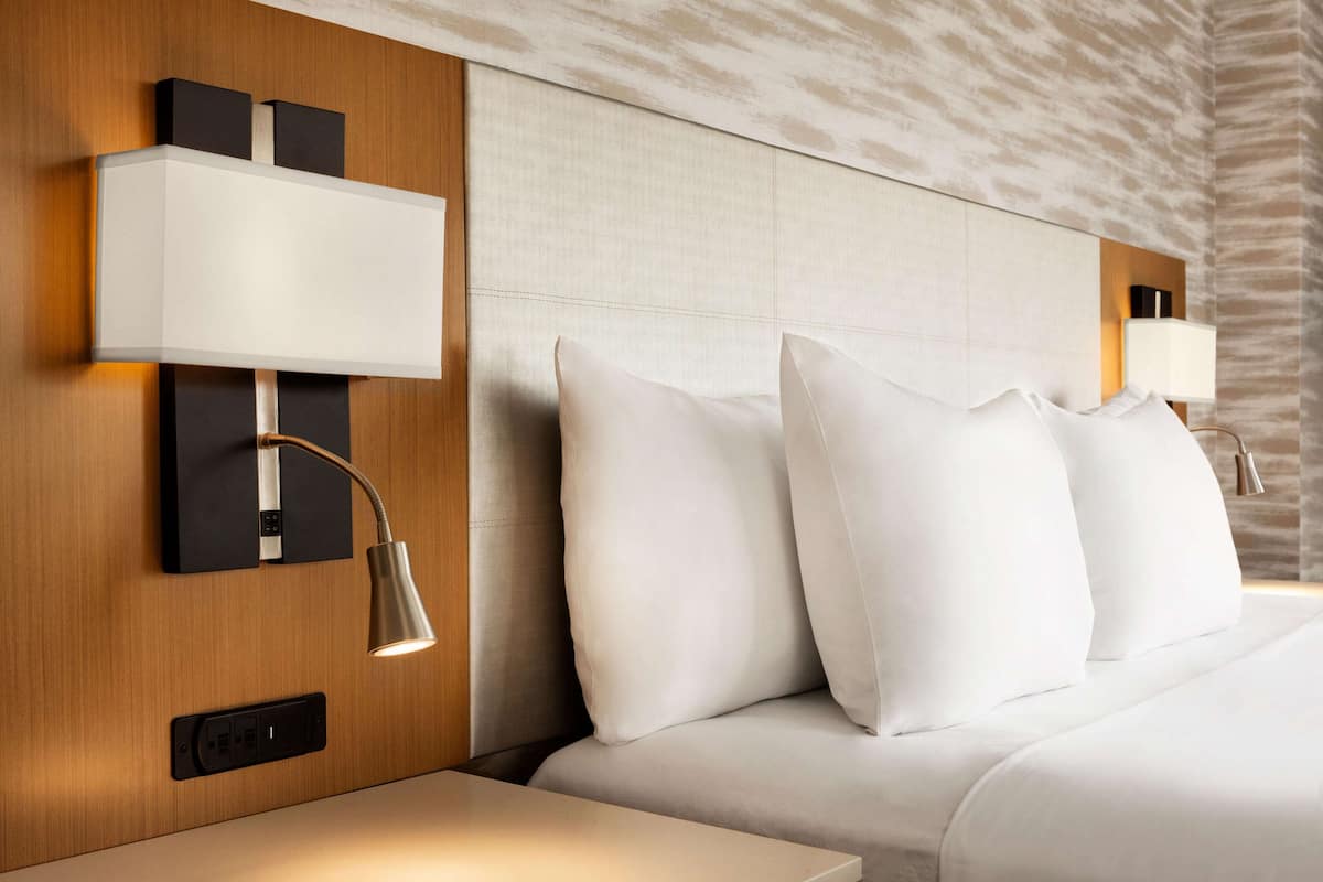 Ein Hotelzimmer mit einem großen Bett, zwei Nachttischlampen und einer wandmontierten Bedienkonsole.