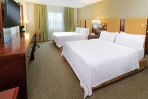 A hotel room with two beds, a desk with a TV, a lamp, and a nightstand with a phone.