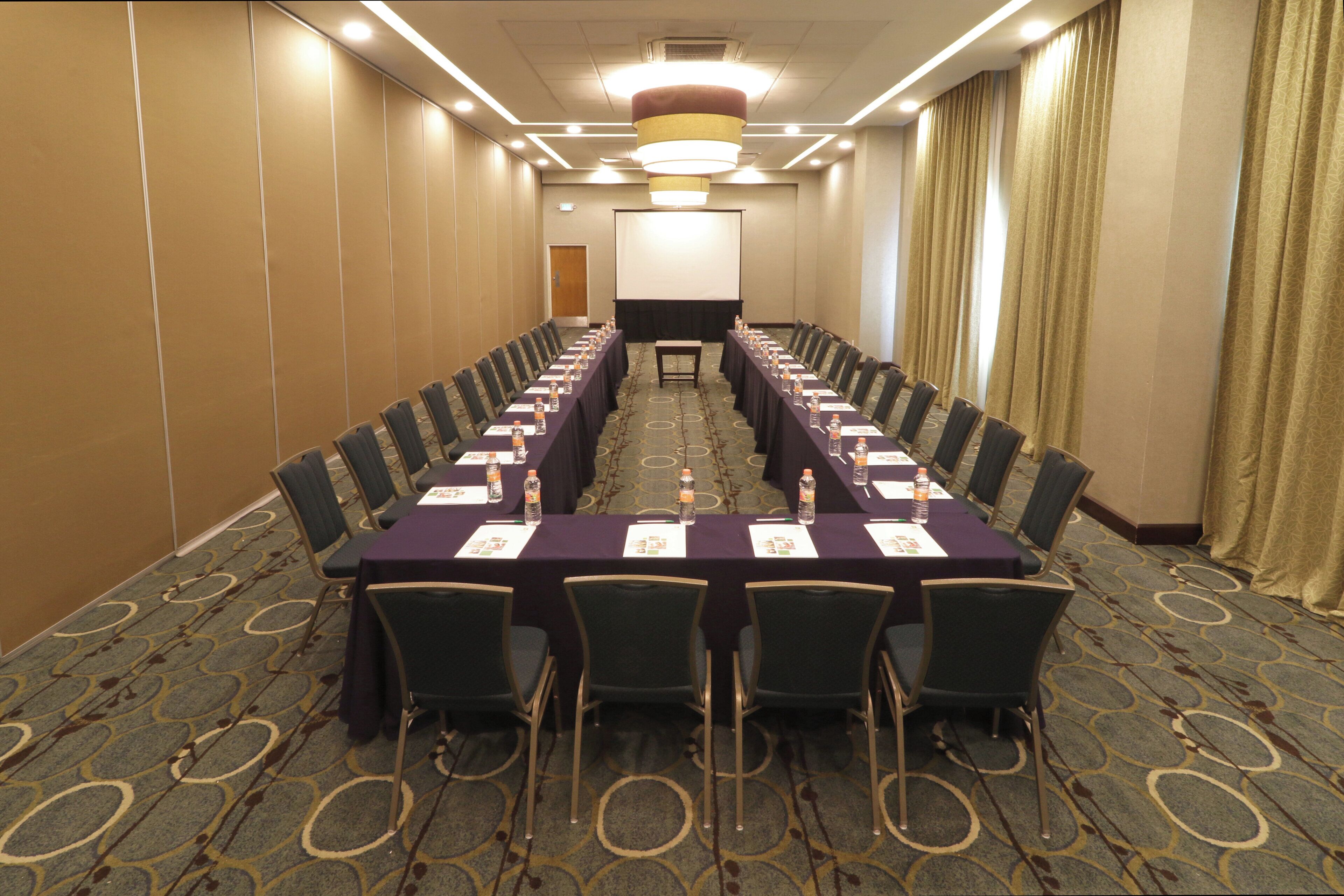Uma sala de conferência com uma mesa comprida, cadeiras e uma tela de projetor.