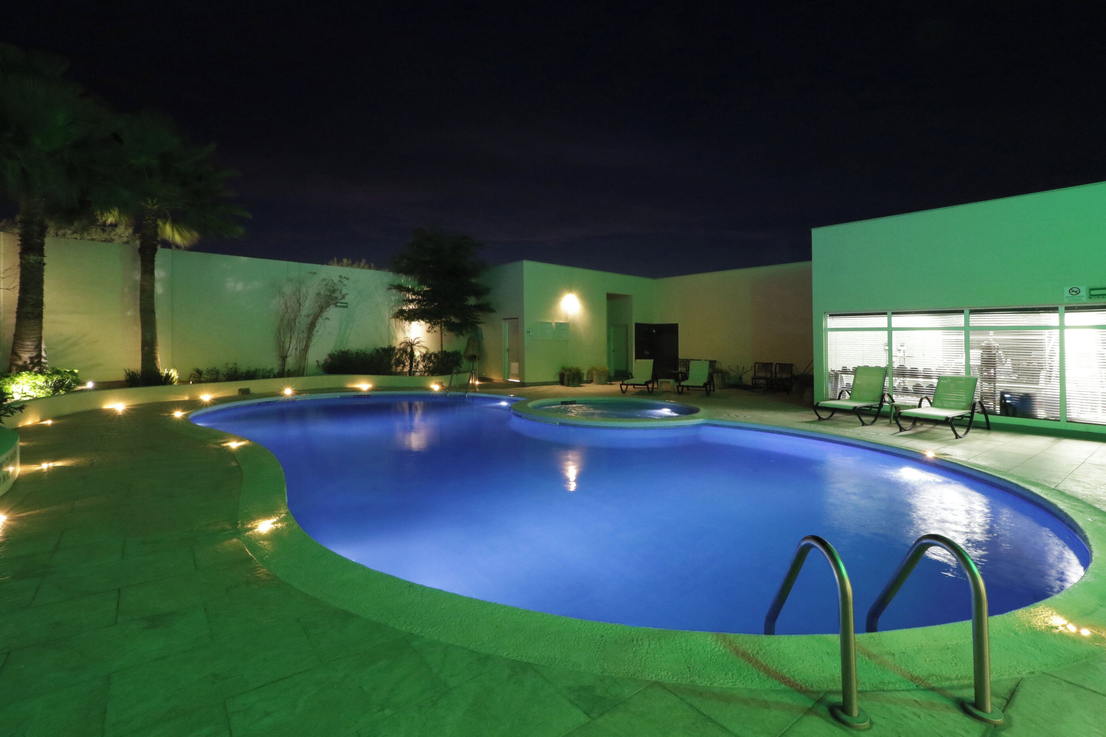 A swimming pool with a curved edge, surrounded by a low wall and a few trees.