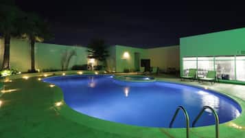 A swimming pool with a curved edge, surrounded by a low wall and a few trees.