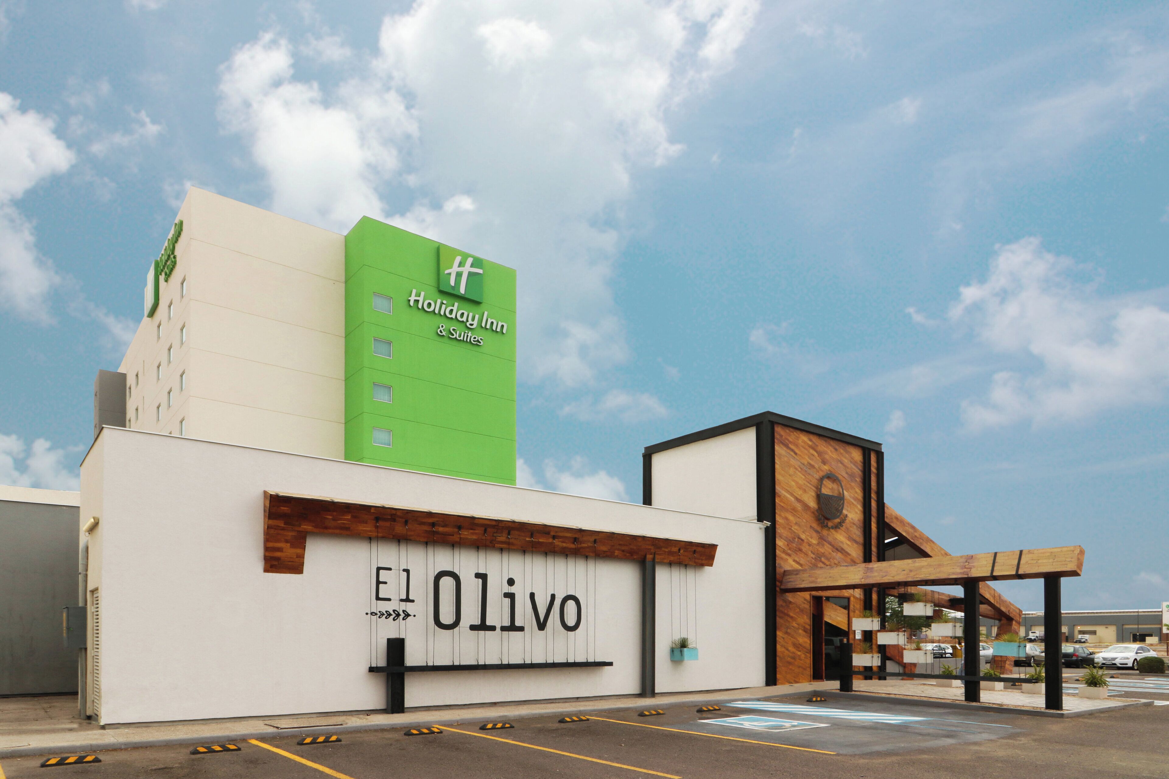 A Holiday Inn & Suites building with a prominent green sign and a white facade.
