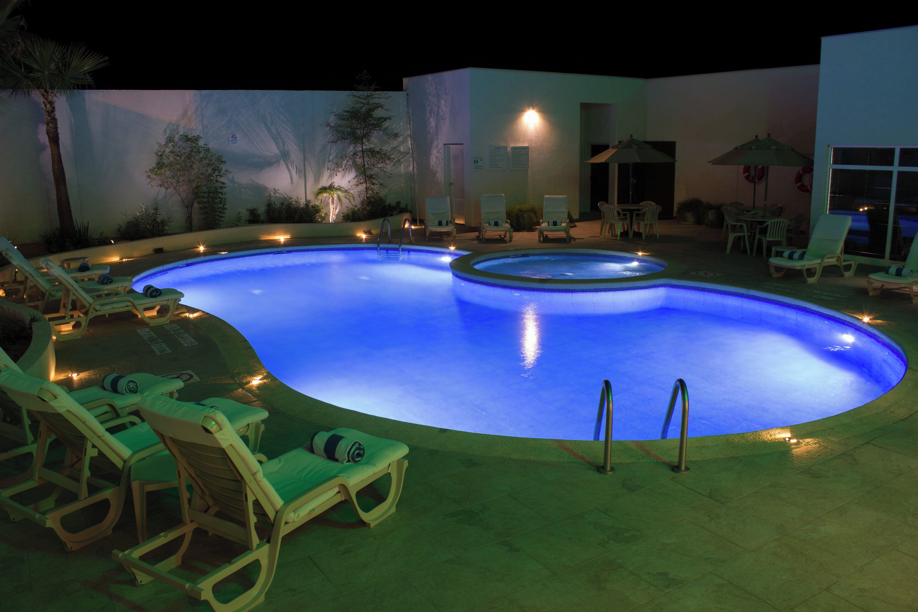 A swimming pool with lounge chairs and umbrellas, surrounded by a landscaped area with plants.