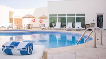 A swimming pool with lounge chairs and umbrellas, a lifebuoy, and a building entrance.