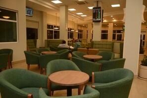 A restaurant with green upholstered chairs and round tables, a TV screen on the wall, and a large window on the left. - Holiday Inn Hotel & Suites Hermosillo Aeropuerto by IHG (Hermosillo)