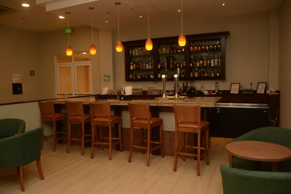 A bar area with wooden bar stools, a counter with a glass display, and hanging pendant lights.
