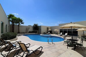 A pool area with lounge chairs and umbrellas, surrounded by a low wall and palm trees. - Holiday Inn Hotel & Suites Hermosillo Aeropuerto by IHG (Hermosillo)