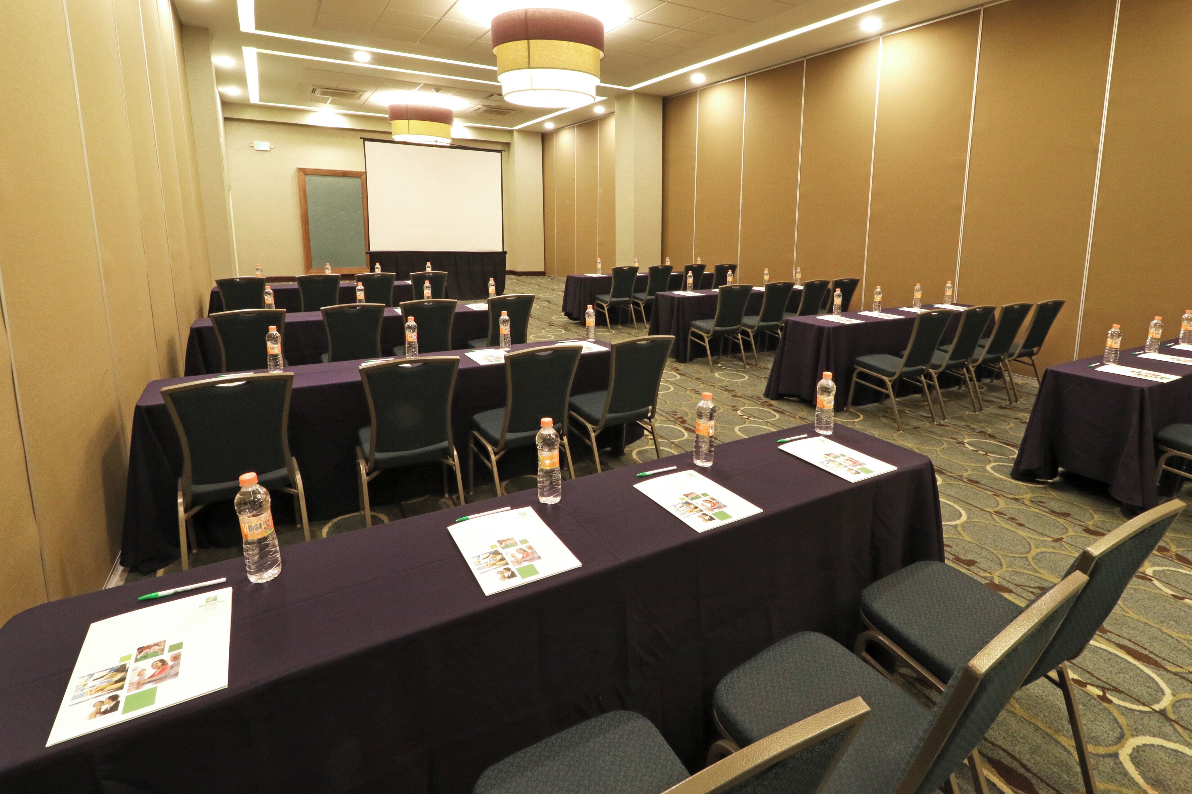 A conference room with rows of tables, chairs, water bottles, and name tags.