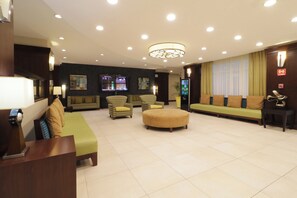 A hotel lobby with a sofa, chairs, a coffee table, and a TV screen. - Holiday Inn Hotel & Suites Hermosillo Aeropuerto by IHG (Hermosillo)