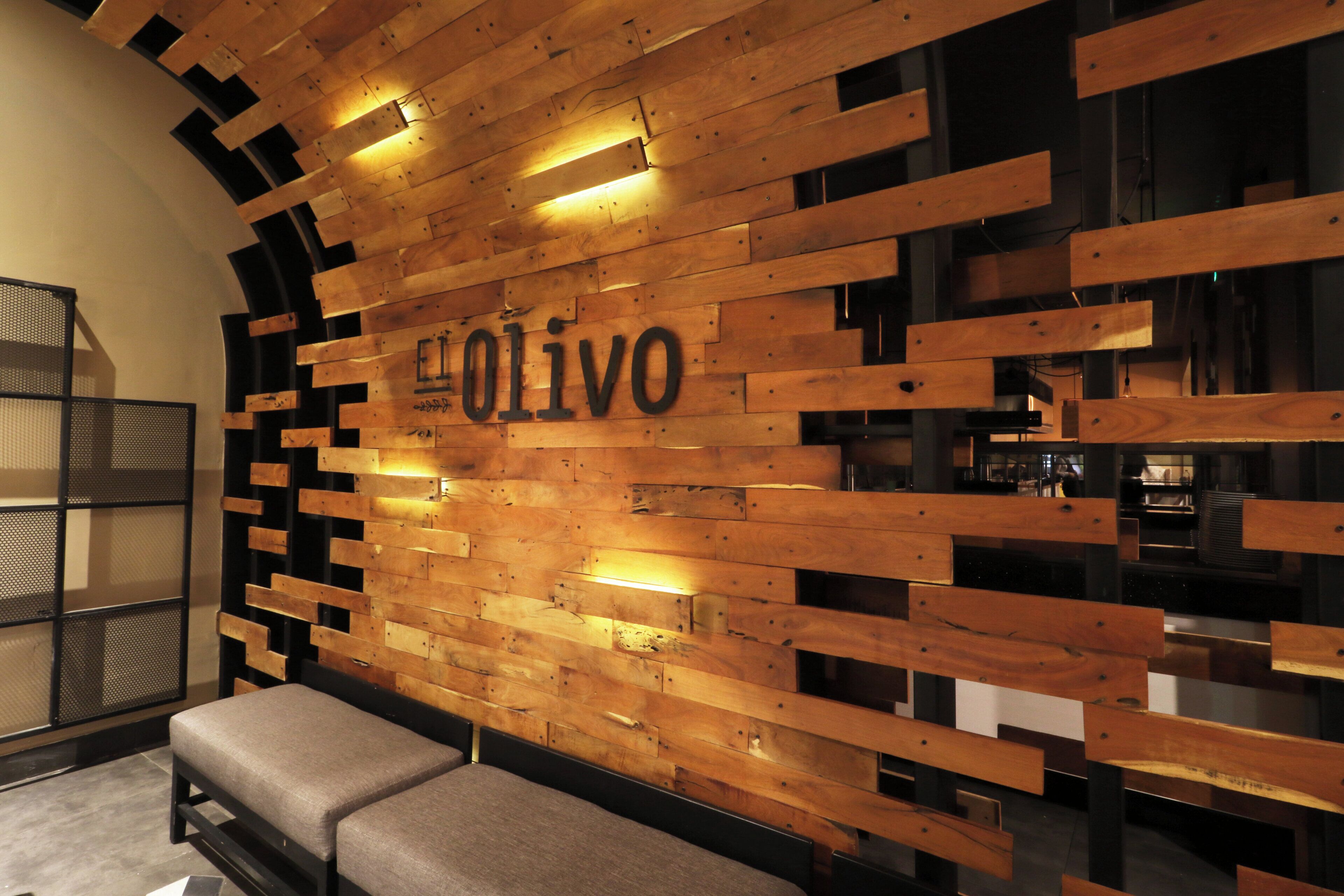 A reception area with a wooden wall displaying the name 'Olivo' and a seating bench.