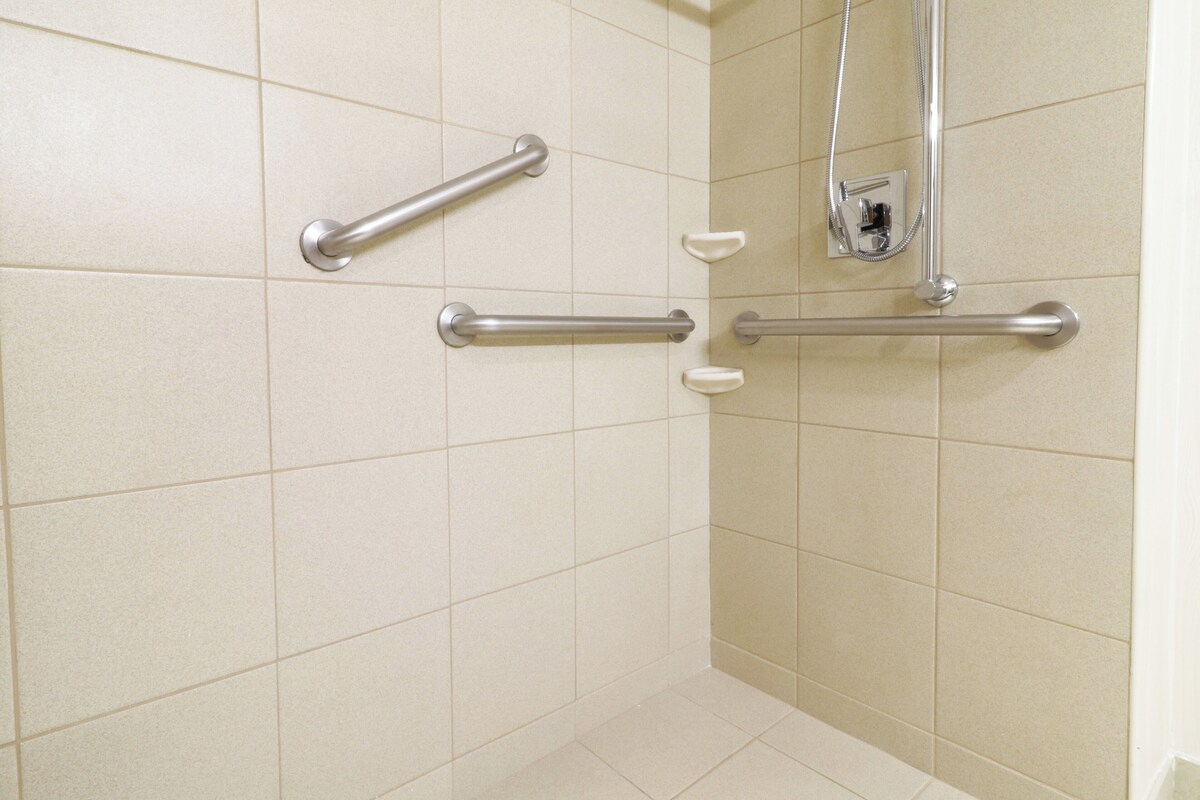 A bathroom with beige tiles, three handrails, and a showerhead.