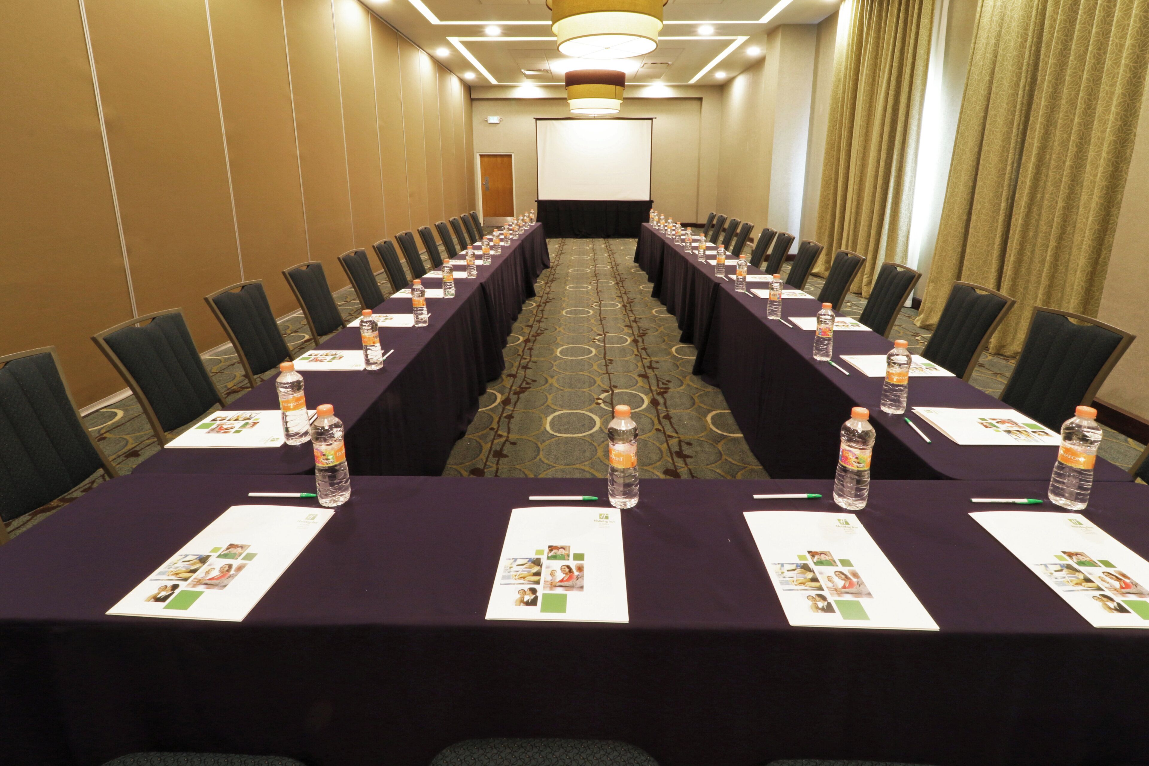 Un salón de conferencias con mesas largas, sillas, botellas de agua y tarjetas de identificación.
