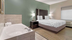 A modern hotel room with a large bed, a separate bathroom with a bathtub, and a nightstand with lamps. - Best Western Casino Inn (Vinton)