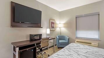 A hotel room with a bed, a desk with a computer, a television, a chair, a lamp, and a window.