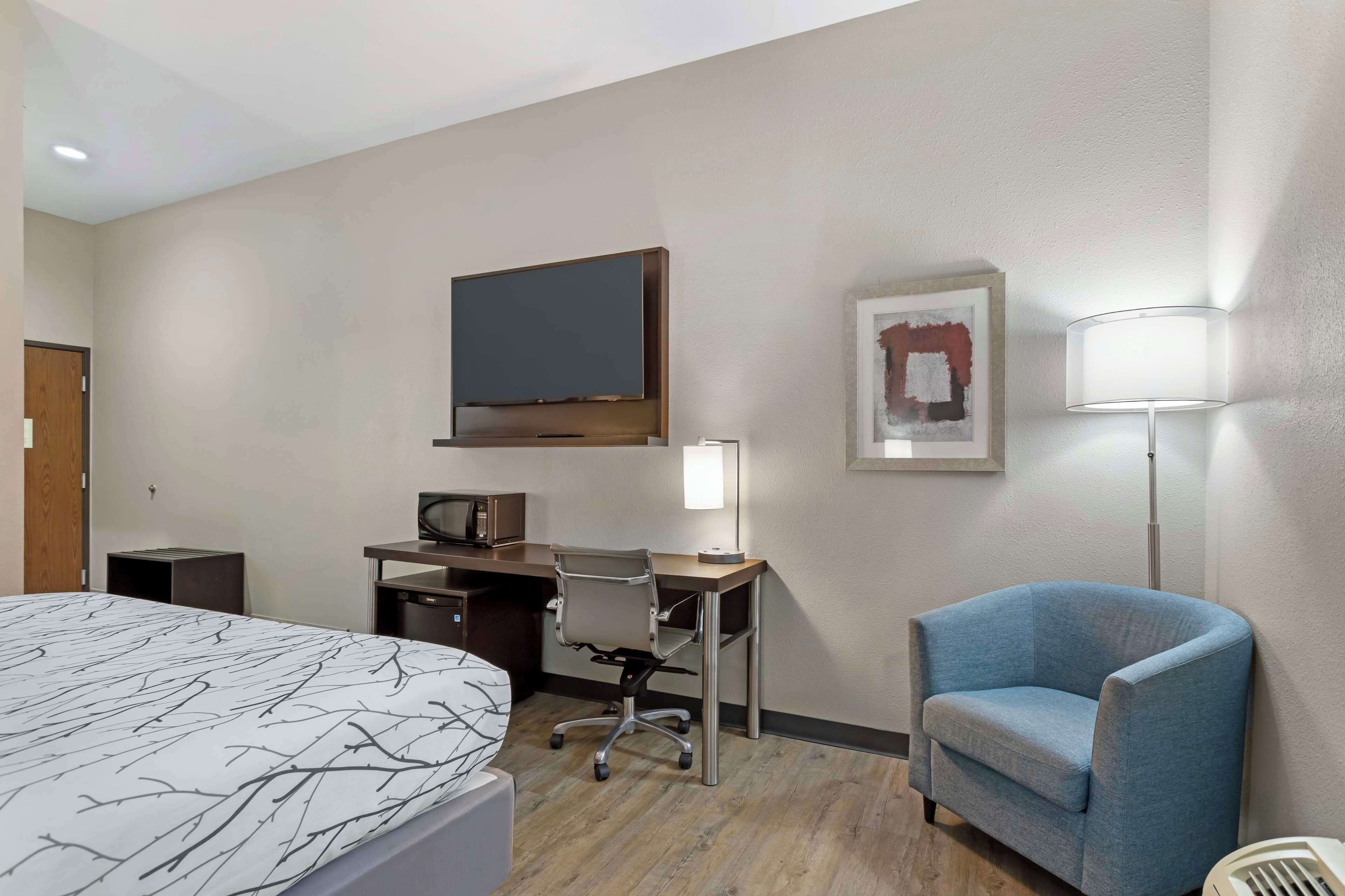 A hotel room with a bed, a desk with a computer, a TV, a chair, and a lamp.