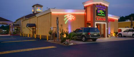 A hotel with a neon sign, a parking lot, and a few cars parked in front.