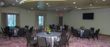 A conference room with round tables, chairs, and a flat-screen TV on the wall.