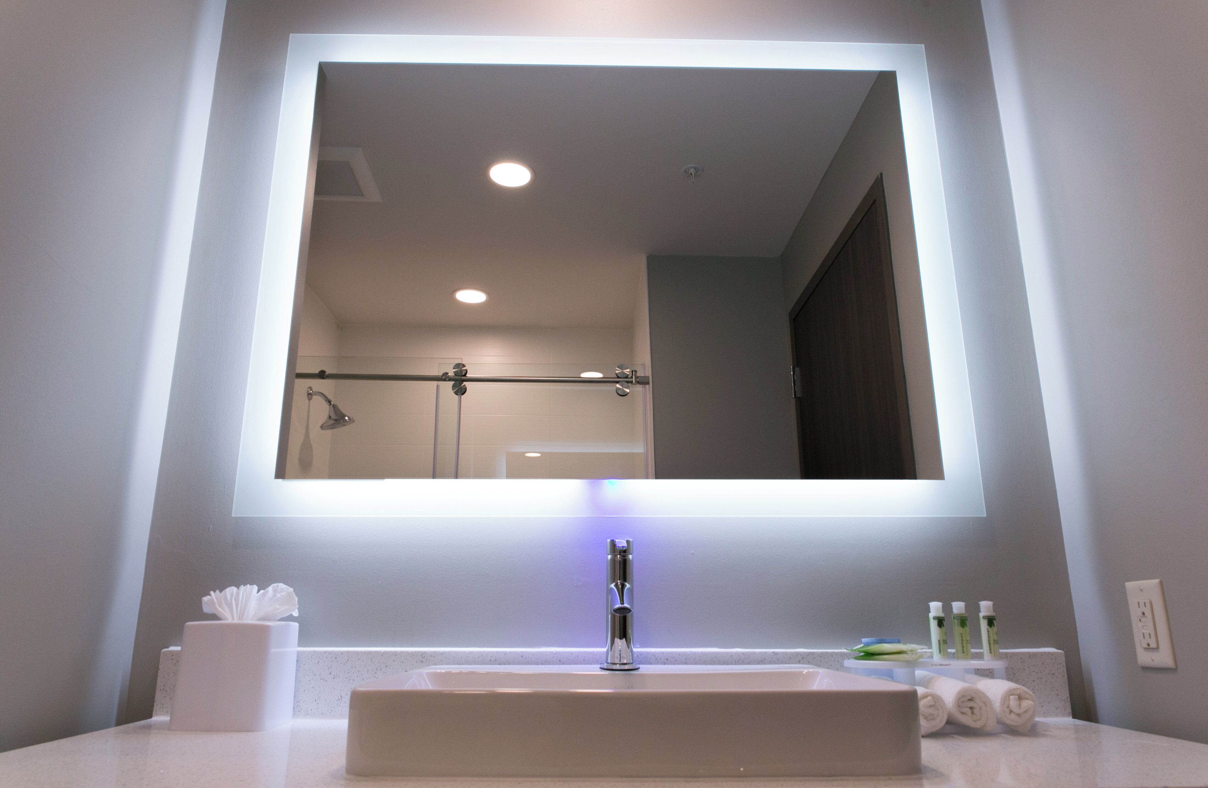 A bathroom with a large mirror, a sink, a towel rack, and a few toiletries.