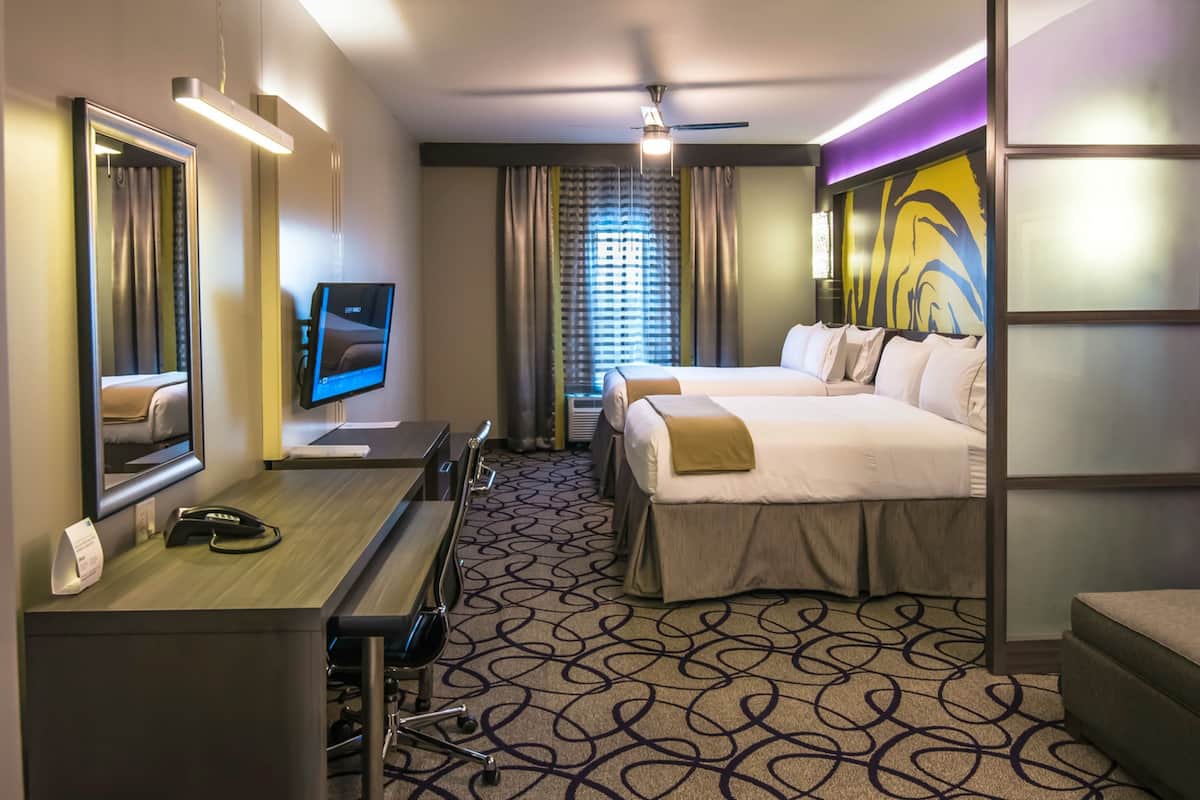 Ein Hotelzimmer mit Schreibtisch, zwei Betten, einem Fernseher und einem großen Spiegel.