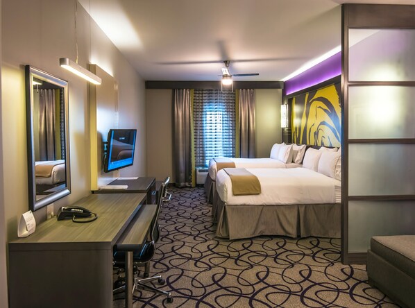 A hotel room with a desk, two beds, a TV, and a large mirror.
