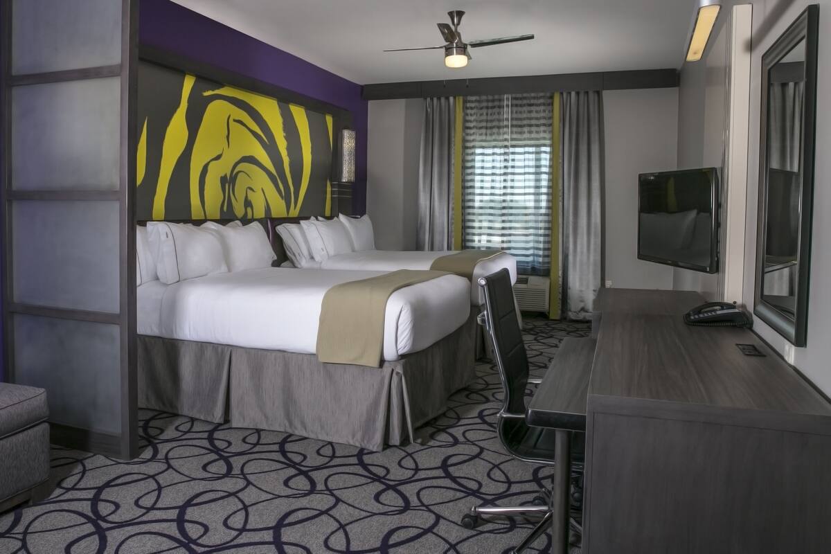 Ein Hotelzimmer mit zwei Betten, einem Schreibtisch, einem Fernseher und einem Deckenventilator.