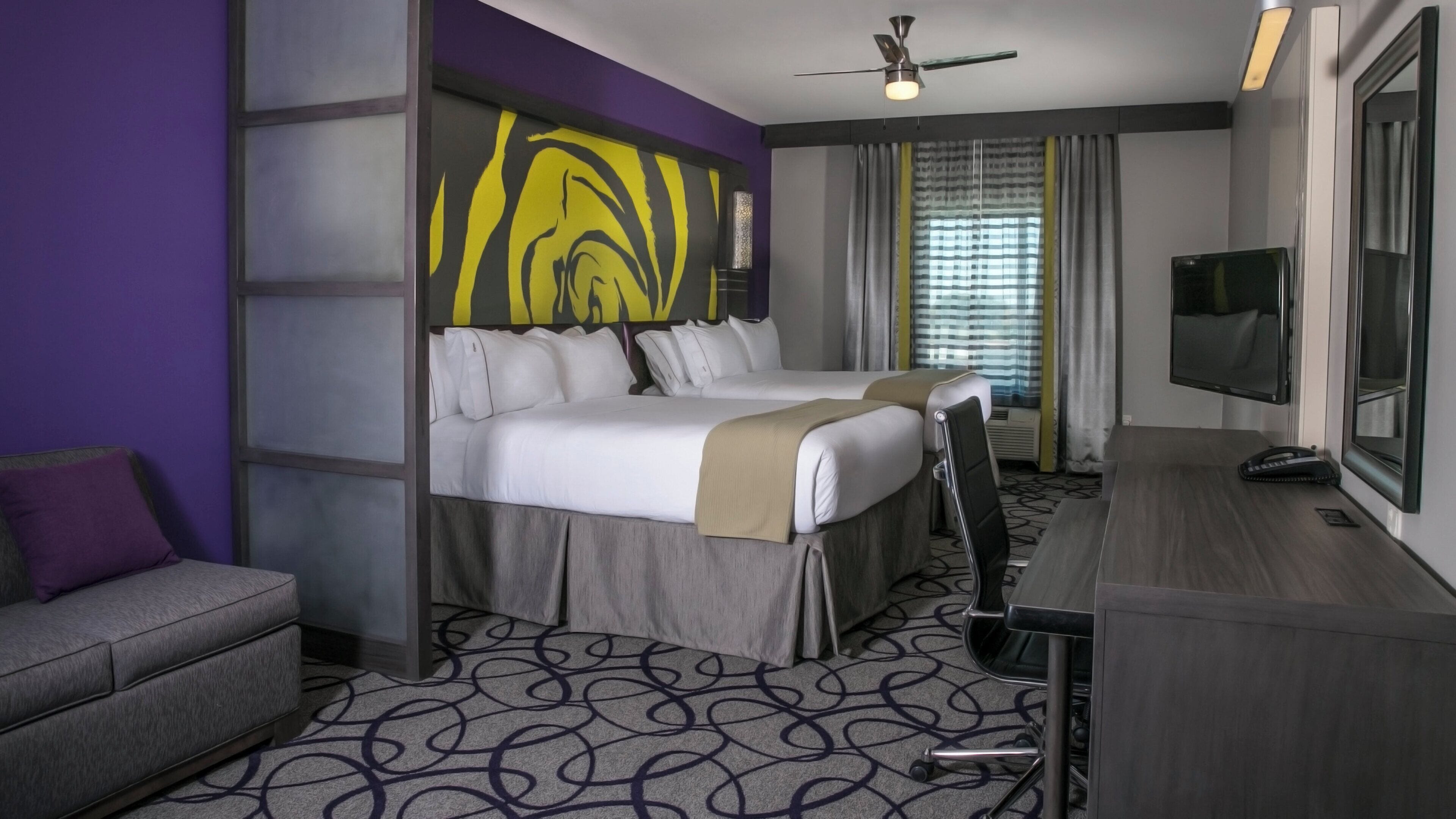 Habitación de hotel con dos camas, un escritorio, un sofá, un televisor y un ventilador de techo.