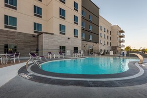 Um hotel moderno com piscina, espreguiçadeiras e área de estar coberta.