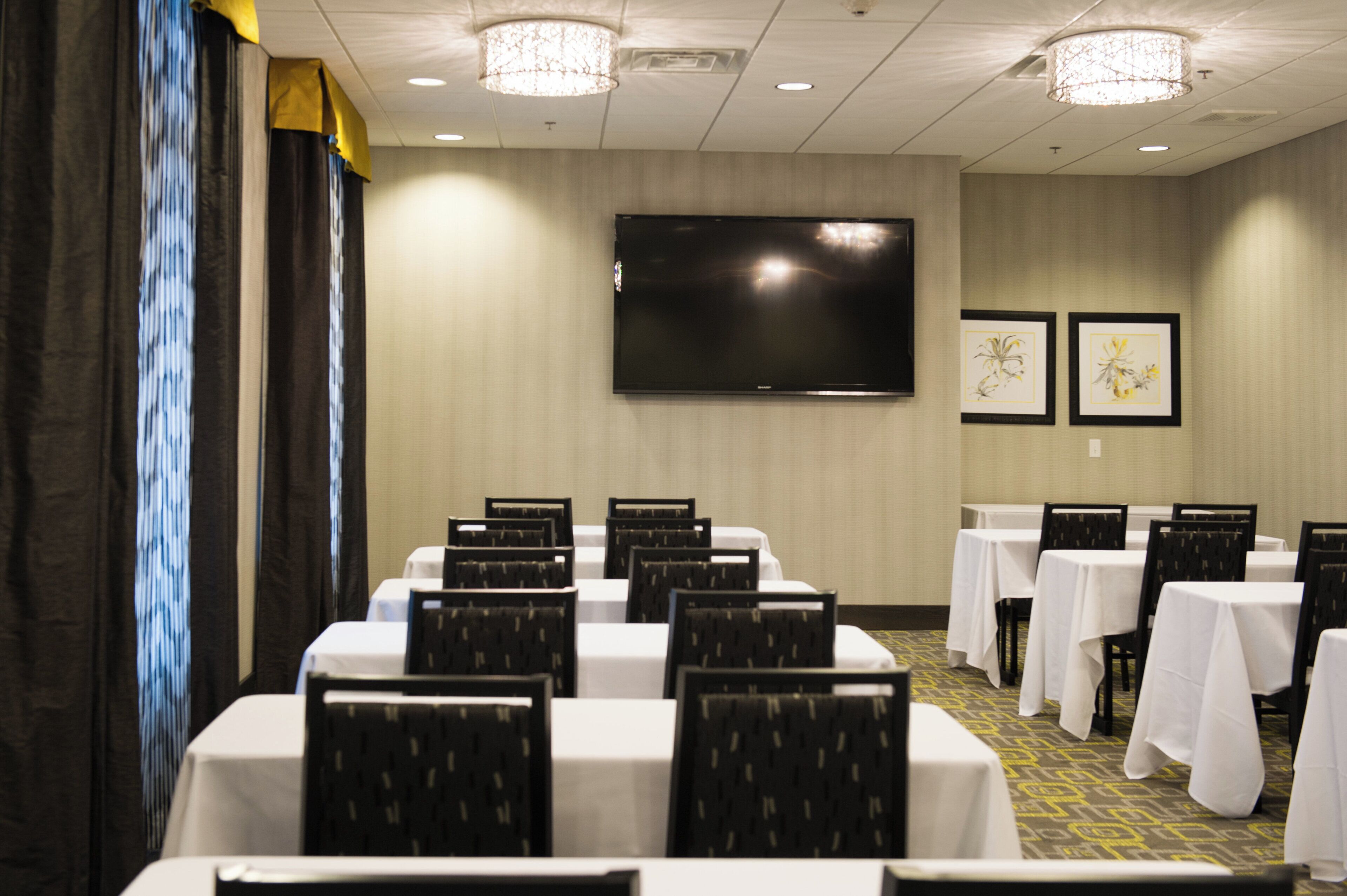 A conference room with tables and chairs, a flat-screen TV, and framed artwork on the wall.