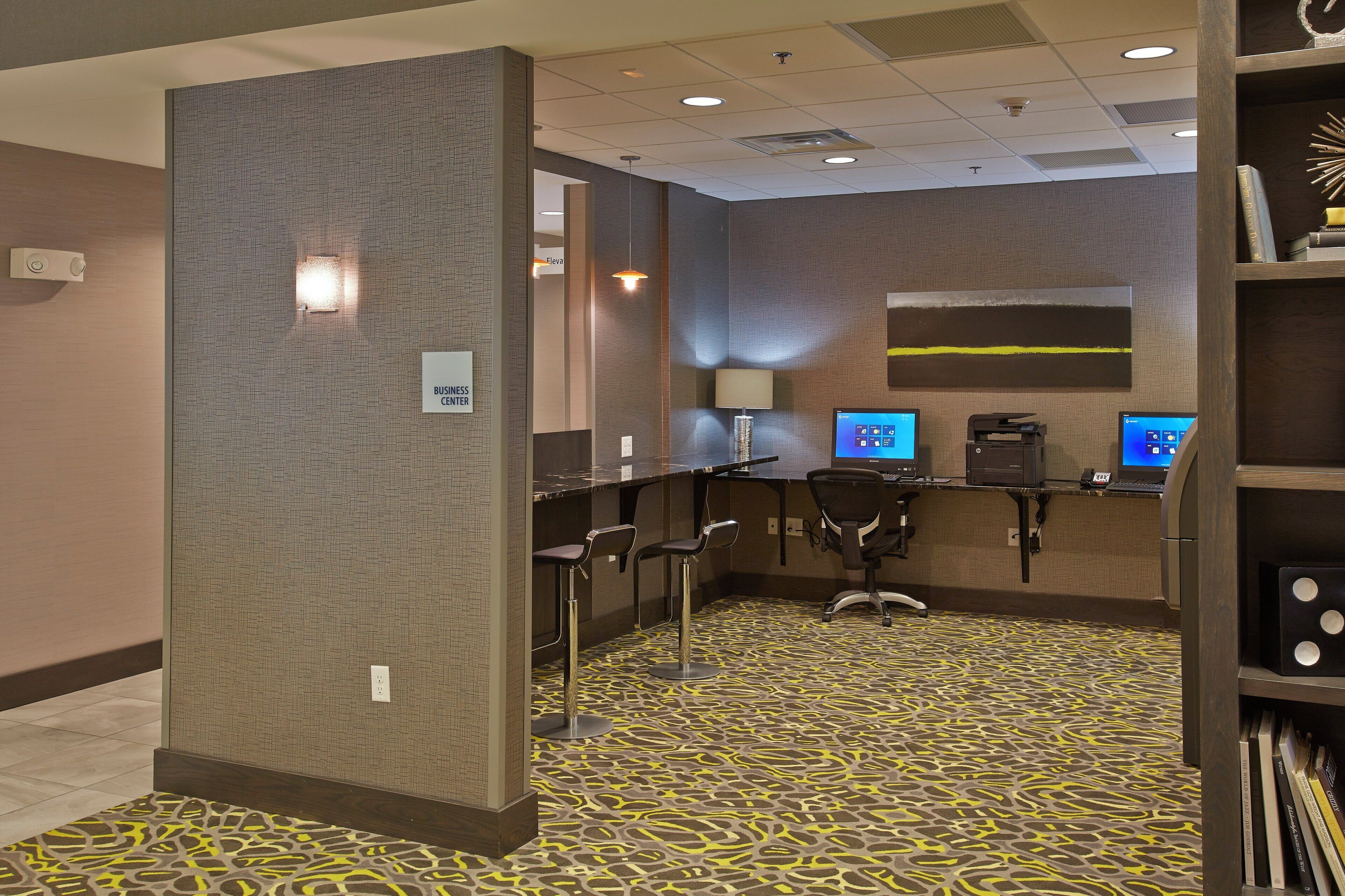 A business center with multiple computer stations, a reception desk, and a bookshelf with books.