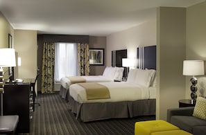 Quarto de hotel com duas camas, uma escrivaninha, uma cadeira, um sofá e uma mesa pequena com abajur.