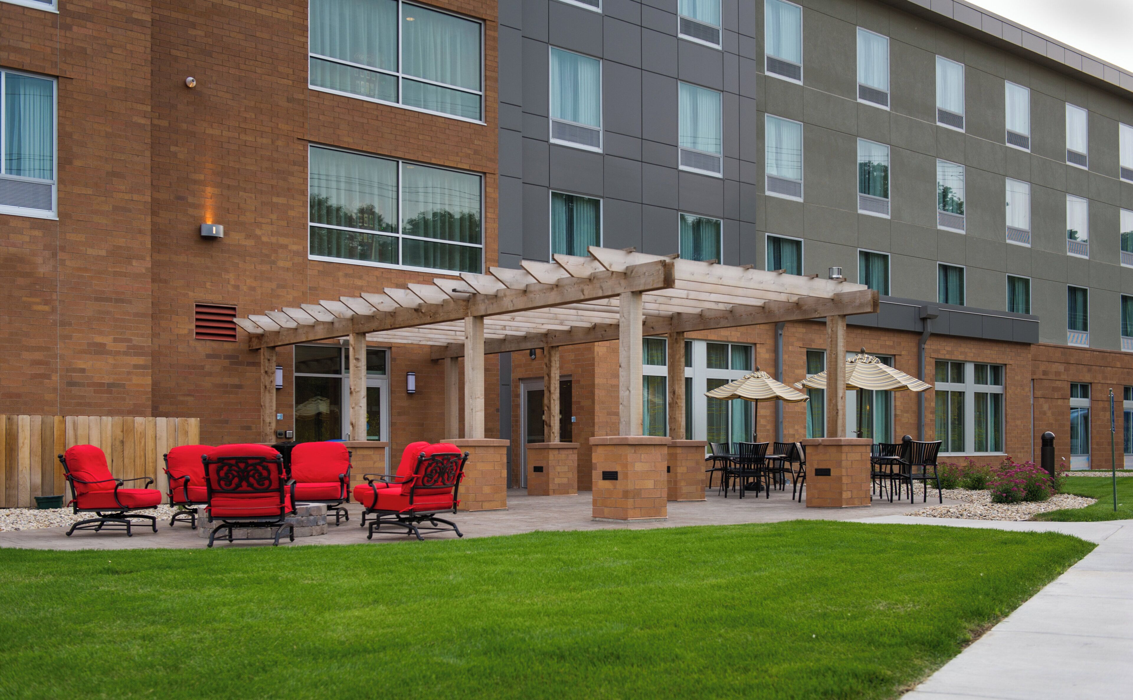 A hotel exterior with a covered patio area, outdoor seating, and a brick facade.