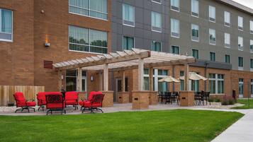 A hotel exterior with a covered patio area, outdoor seating, and a brick facade.