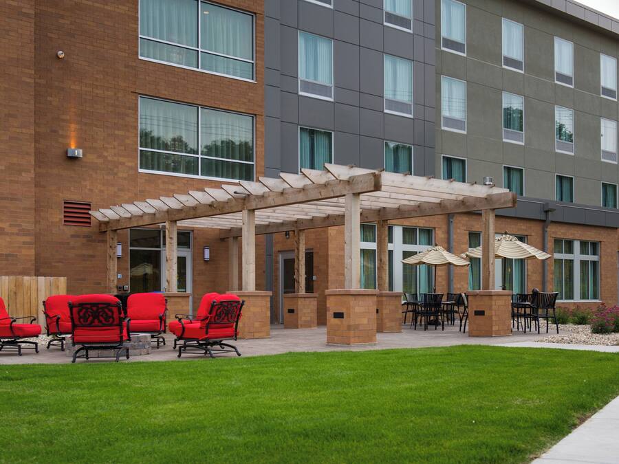 A hotel exterior with a covered patio area, outdoor seating, and a brick facade.