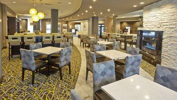 A hotel lobby with multiple seating areas, a reception desk, and a television screen mounted on a stone wall.