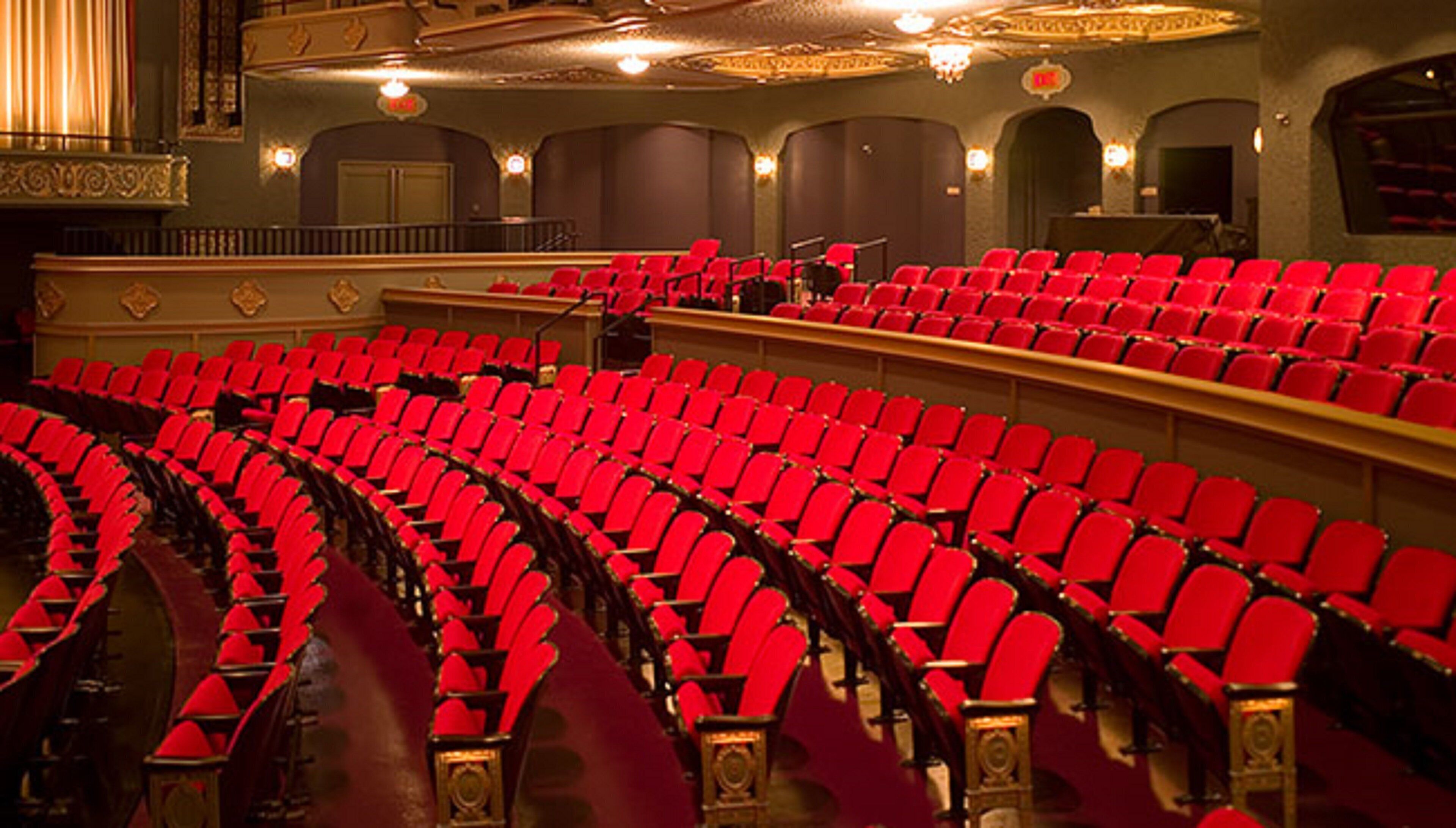 Un auditorio interior con hileras de asientos rojos y detalles arquitectónicos ornamentales.