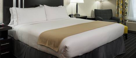 Habitación de hotel con una cama grande, un escritorio con lámpara, una silla y una ventana con cortinas.