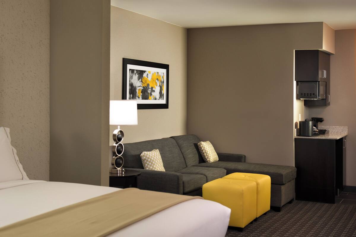 A hotel room with a bed, a sofa, a coffee machine, and a framed picture on the wall.