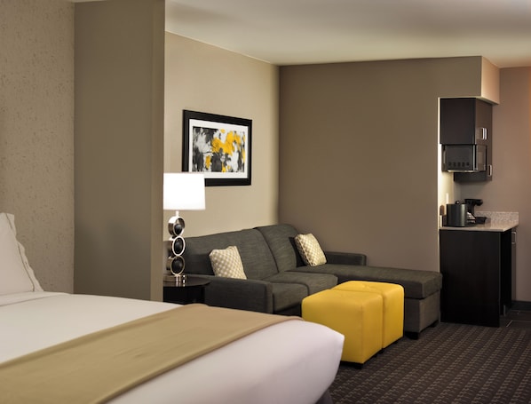 Quarto de hotel com cama, sofá, máquina de café e uma moldura na parede.