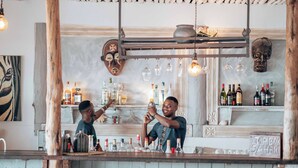 A bar area with wooden beams, shelves of bottles, and a 'TIP BOX SAHARI' sign. - Sahari Zanzibar (Bwejuu)