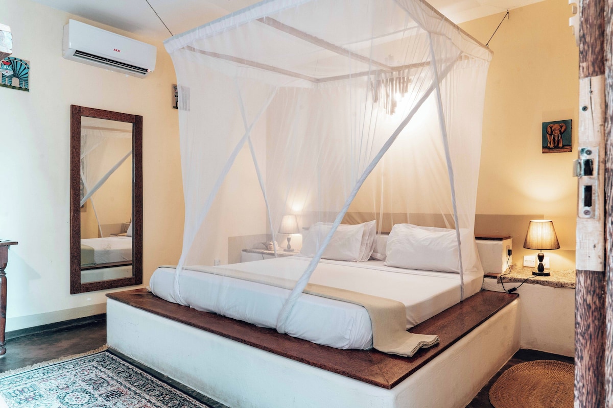 Un dormitorio con cama bajo dosel, lámparas de noche, un espejo y aire acondicionado instalado en la pared.