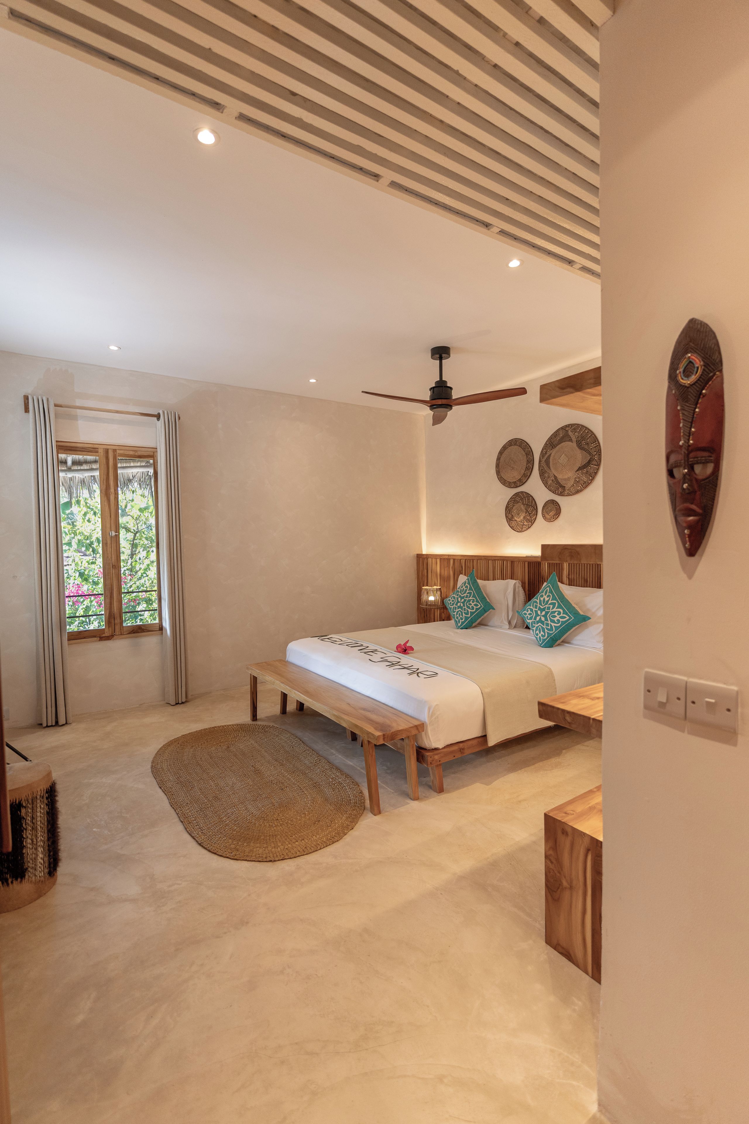 Quarto com cama, ventilador de teto, janela com cortinas e parede decorada com pratos.