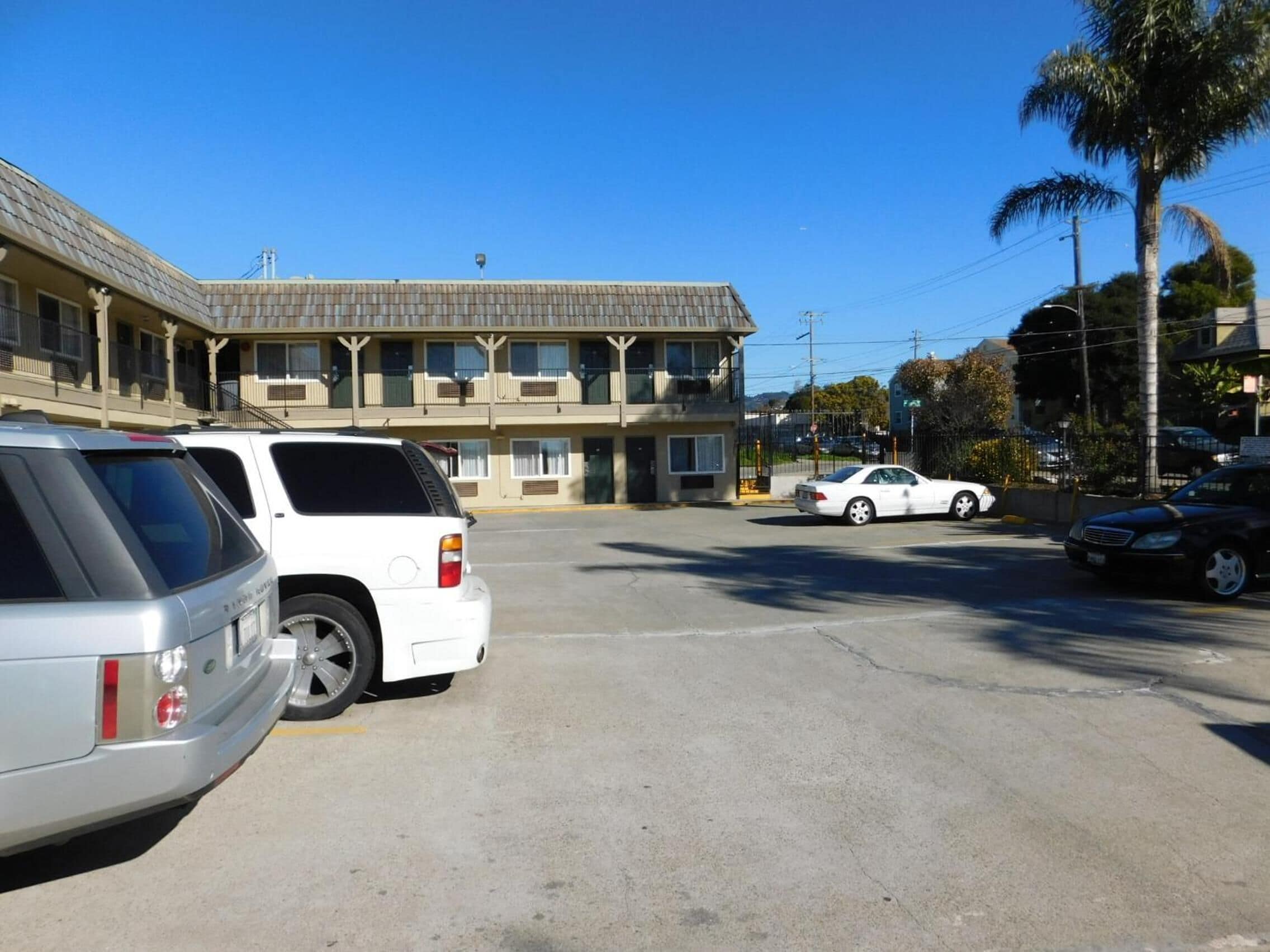 A motel with a parking lot, a white SUV, and a white sedan parked in front.