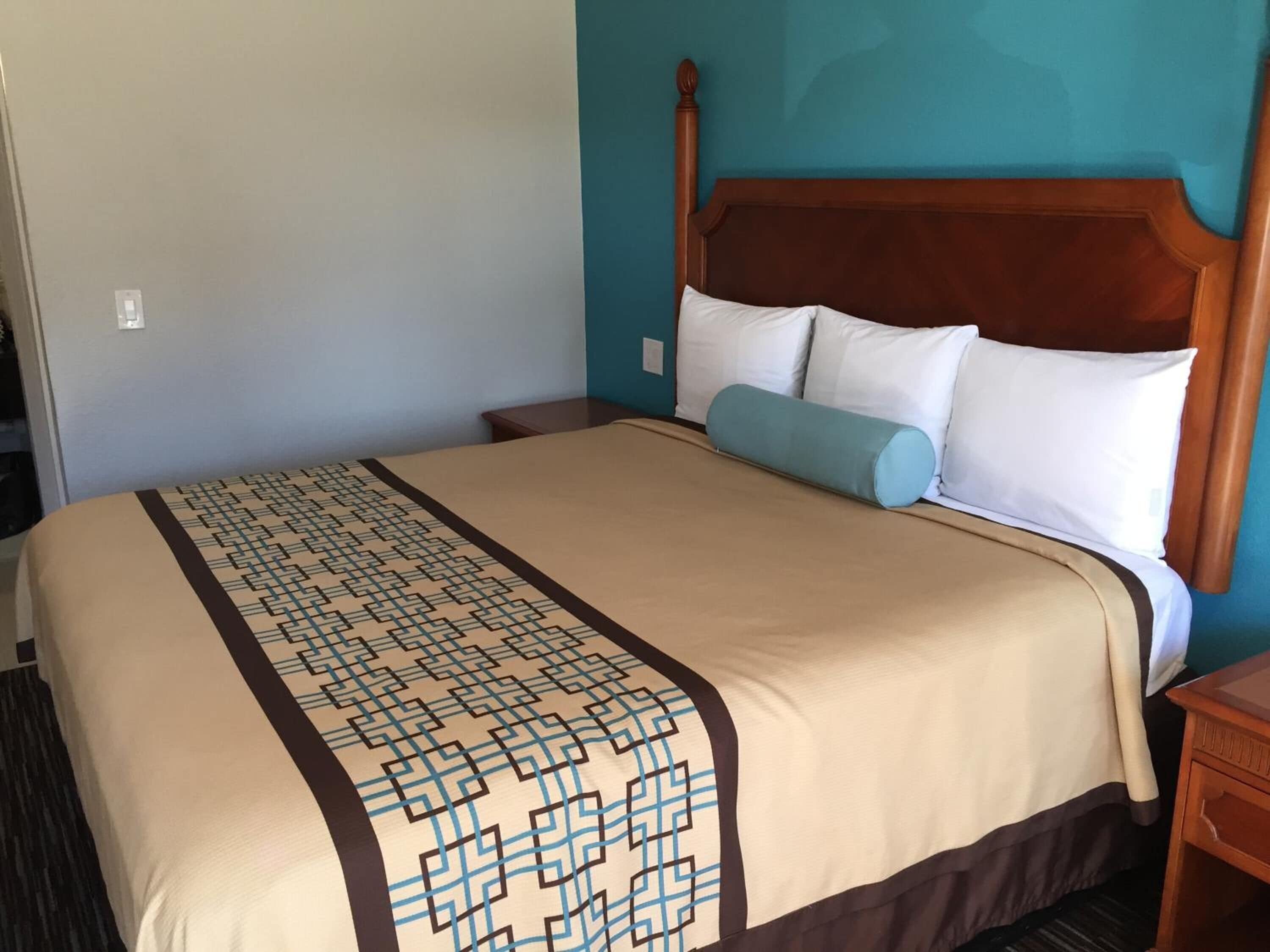 Una habitación de hotel con una cama grande, cabecera de madera y colcha estampada.