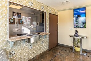 A reception area with a mosaic tile wall, a reception desk, a door, a welcome poster, and a small potted plant. - Continental Lodge (Oakland)
