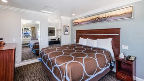 A hotel room with a large bed, a wooden headboard, a nightstand with a phone, and a painting on the wall. - Continental Lodge (Oakland)