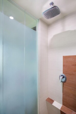 A modern bathroom with a glass shower enclosure, a wooden vanity, and a wall-mounted showerhead. - Business Hotel Tomang (Jakarta)