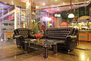 A lobby with two black leather sofas, a glass coffee table, and a statue of the Statue of Liberty. - Business Hotel Tomang (Jakarta)