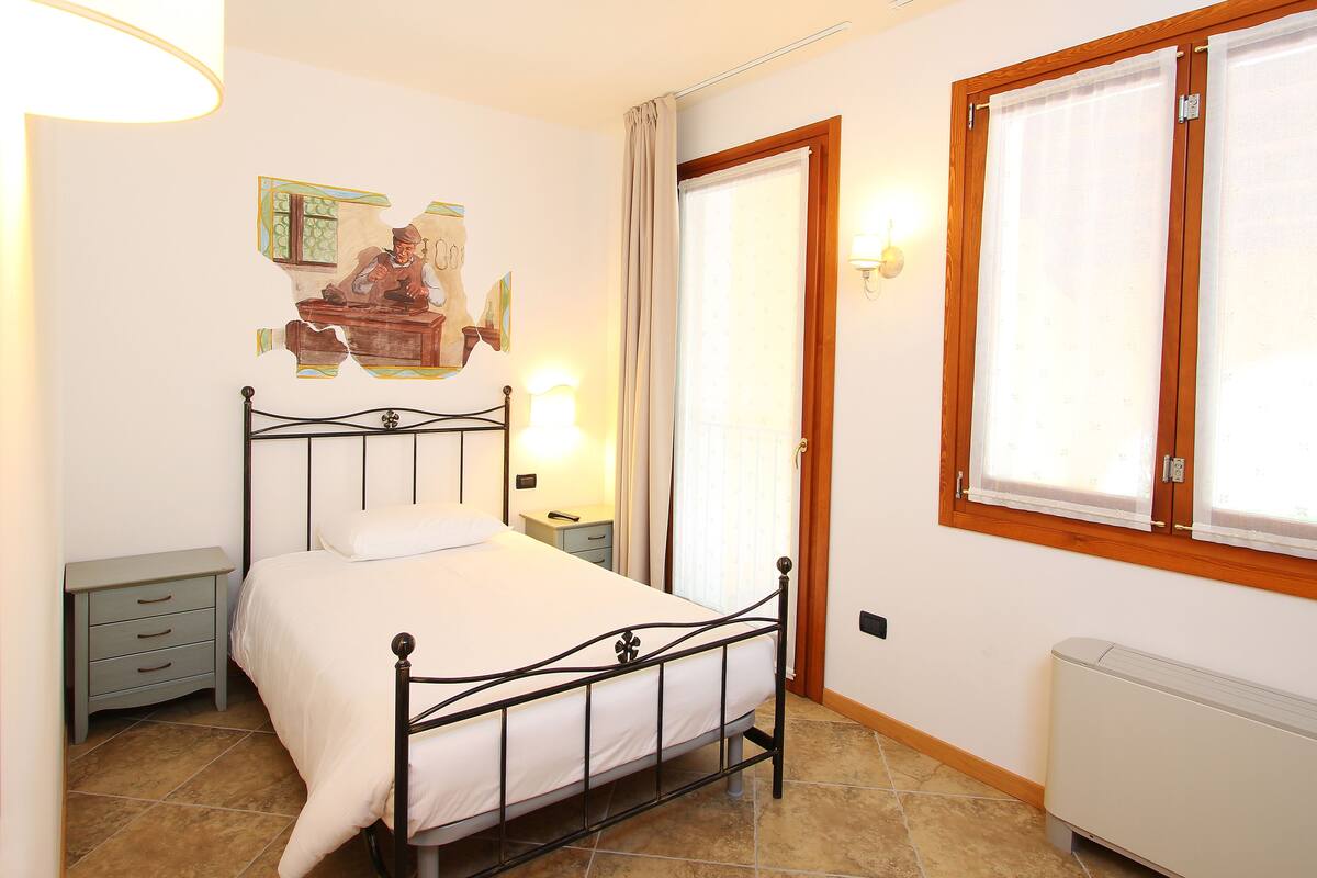A bedroom with a bed, nightstand, wall art, window, and radiator.